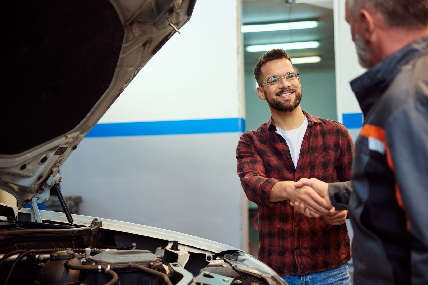 A smiling male customer talking and doing a handshake with a mechanic