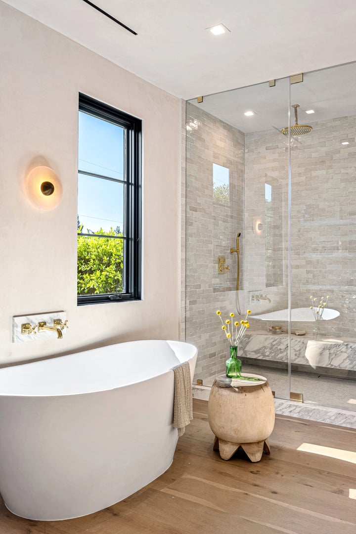 Modern bathroom with a freestanding tub, glass shower, and wooden accents, featuring natural light and elegant decor.