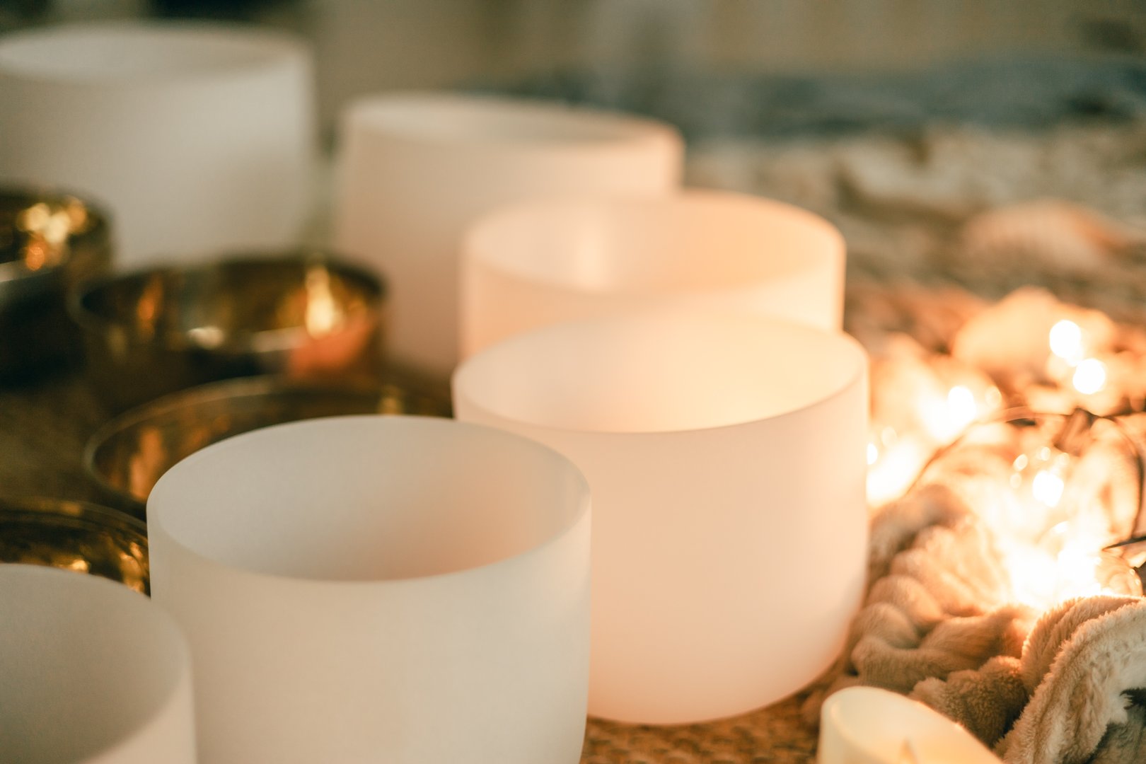 Warm close-up of glowing crystal singing bowls with candle light and gold tones, symbolizing relaxation, balance, and feminine energy.