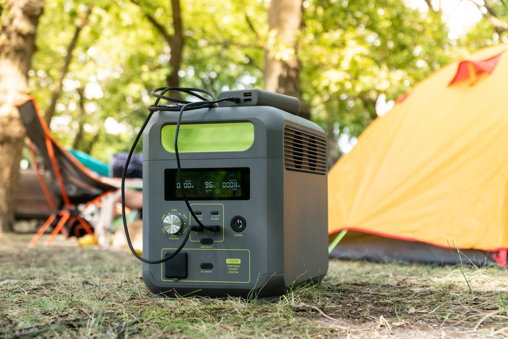 Portable power station with lithium ferrophosphate battery  charging electronic  devices used at a wild camp site,  in front  of yellow tent. Portable electric power  and tourism concept