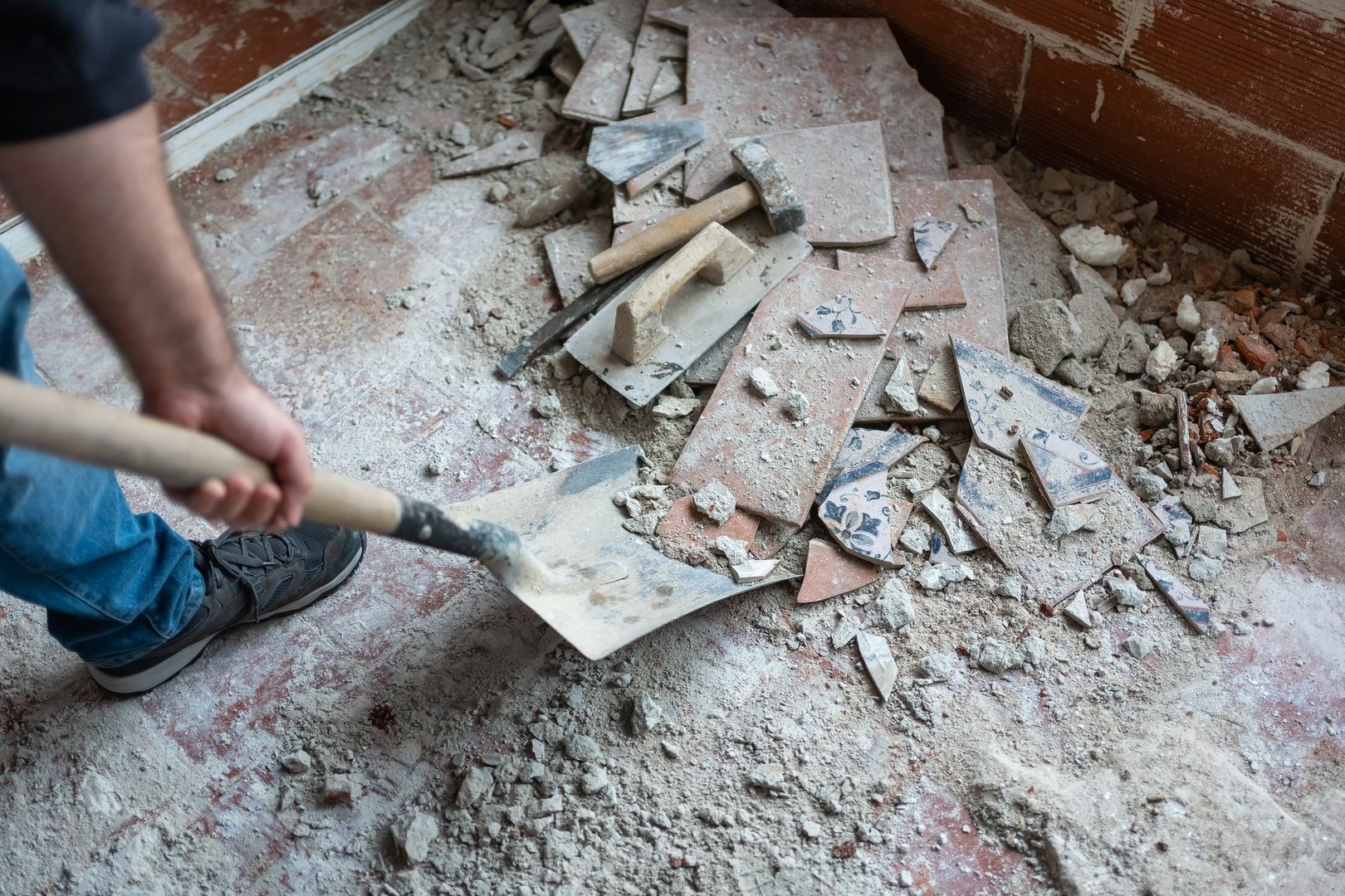 Arbeiter sammelt Bauschutt mit Schaufel nach Abbrucharbeiten