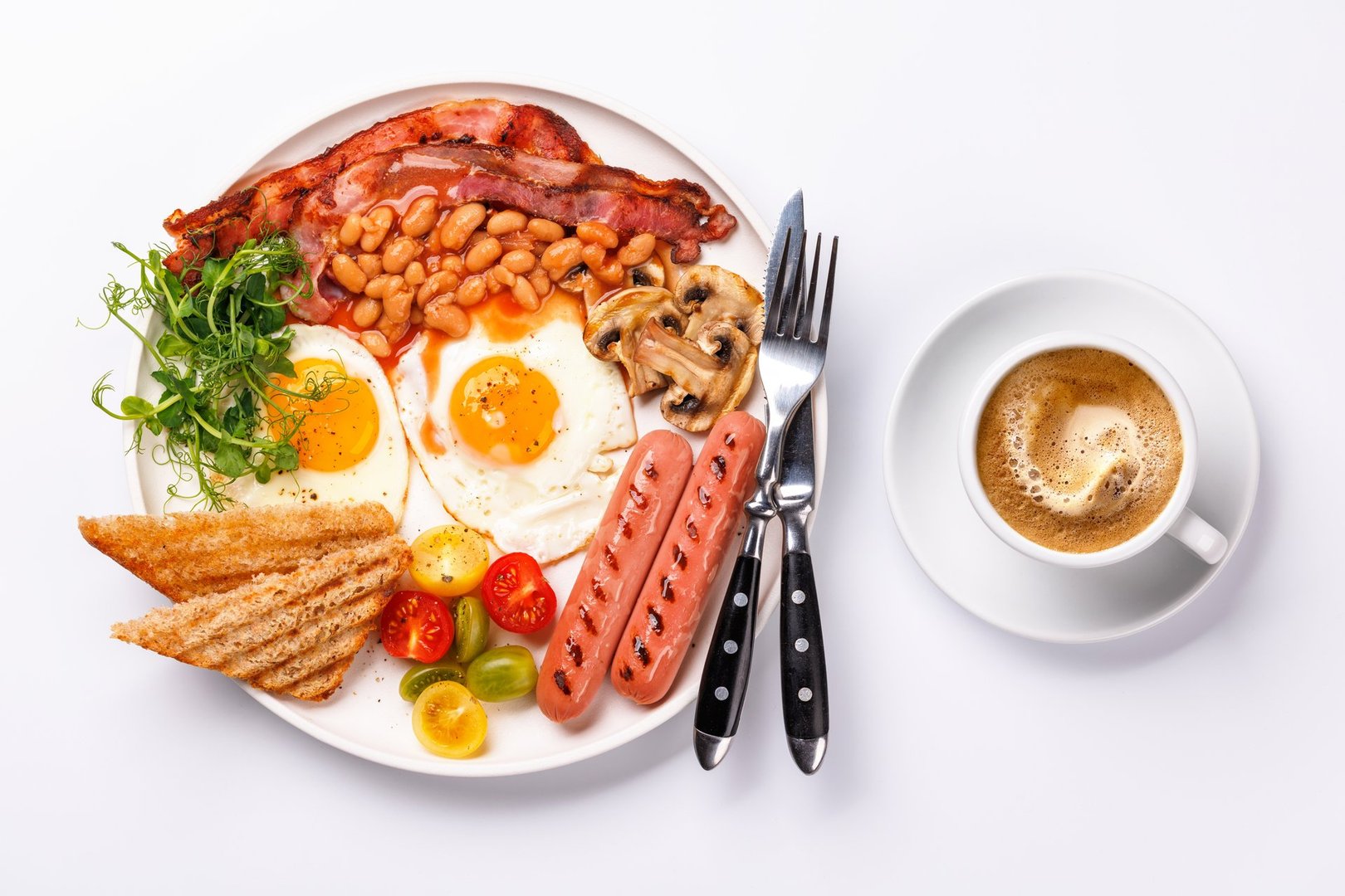 A classic breakfast plate featuring sunny-side-up eggs, crispy bacon, sausages, and fresh tomatoes, served with a hot cup of coffee for a hearty start to the day
