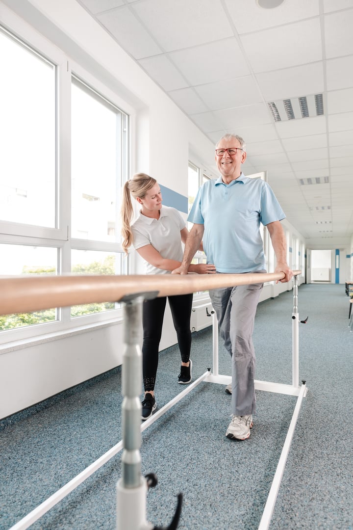 Senior Patient and physical therapist in rehabilitation walking exercises, she is helping him along the bars