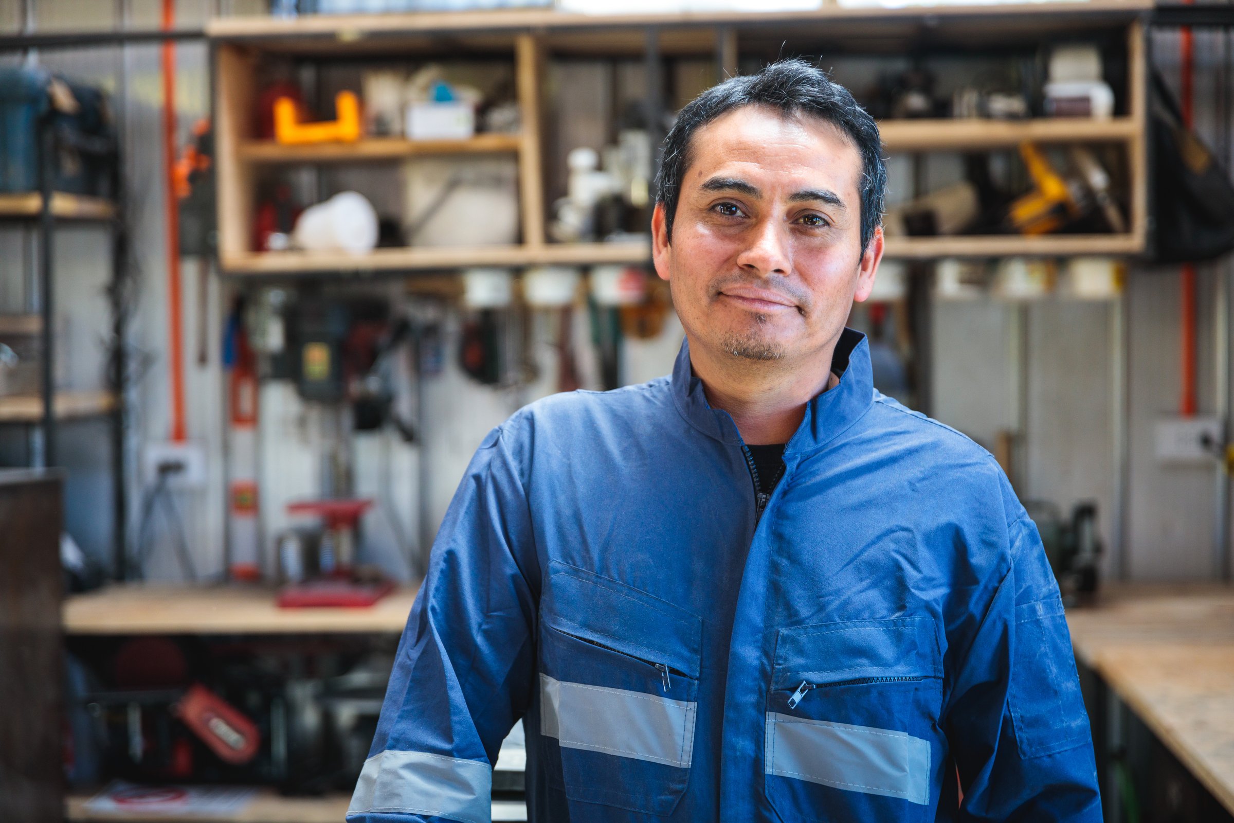 Portrait of a latin worker smiling in his workshop, shelves with tools in the background