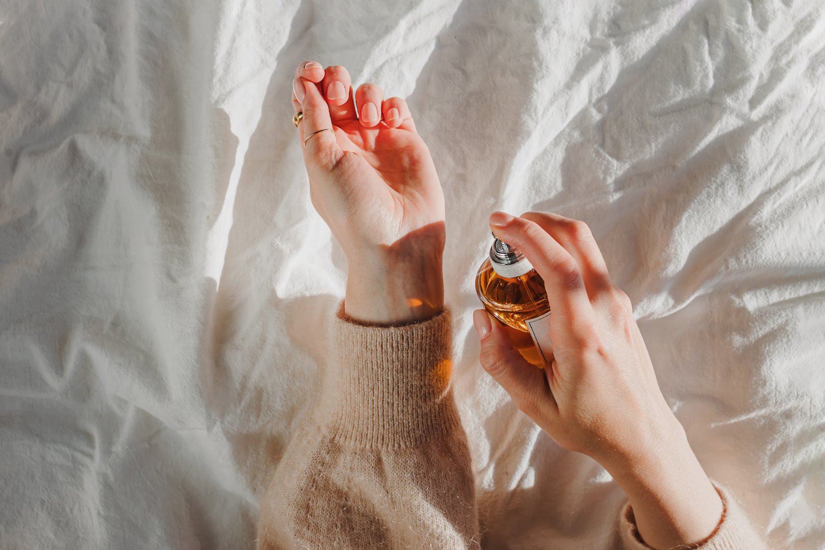 Female hands holding a bottle of perfume in natural morning light, overhead view