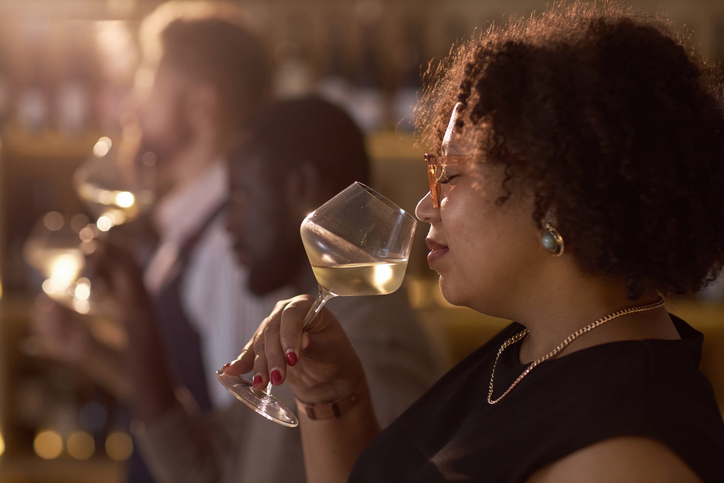 Medium close up of mixed race mature woman enjoying floral wine scent during degustation