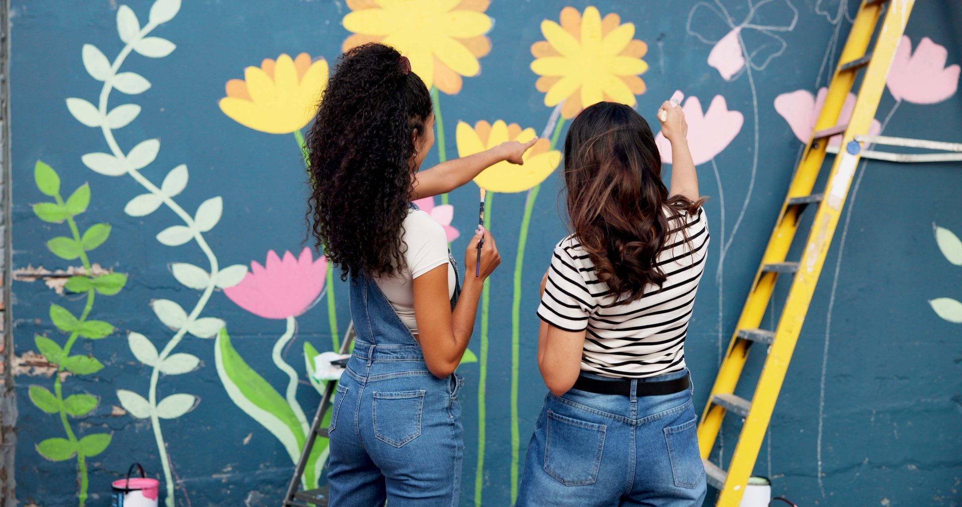 Women, teamwork or planning painting on wall for mural, drawing flowers or community service at building. Artist, back or girls with ladder for floral decoration, renovation or project for design