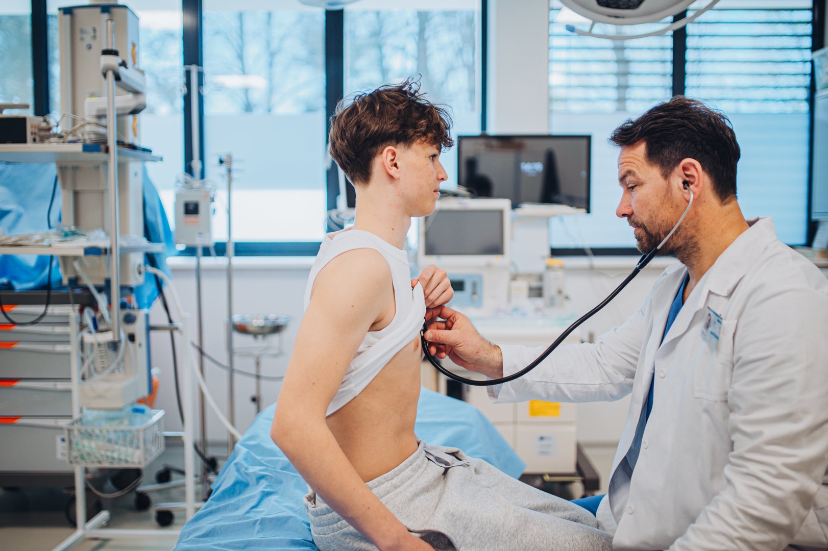 Teen boy undergoing medical checkup with smiling doctor in hospital room.