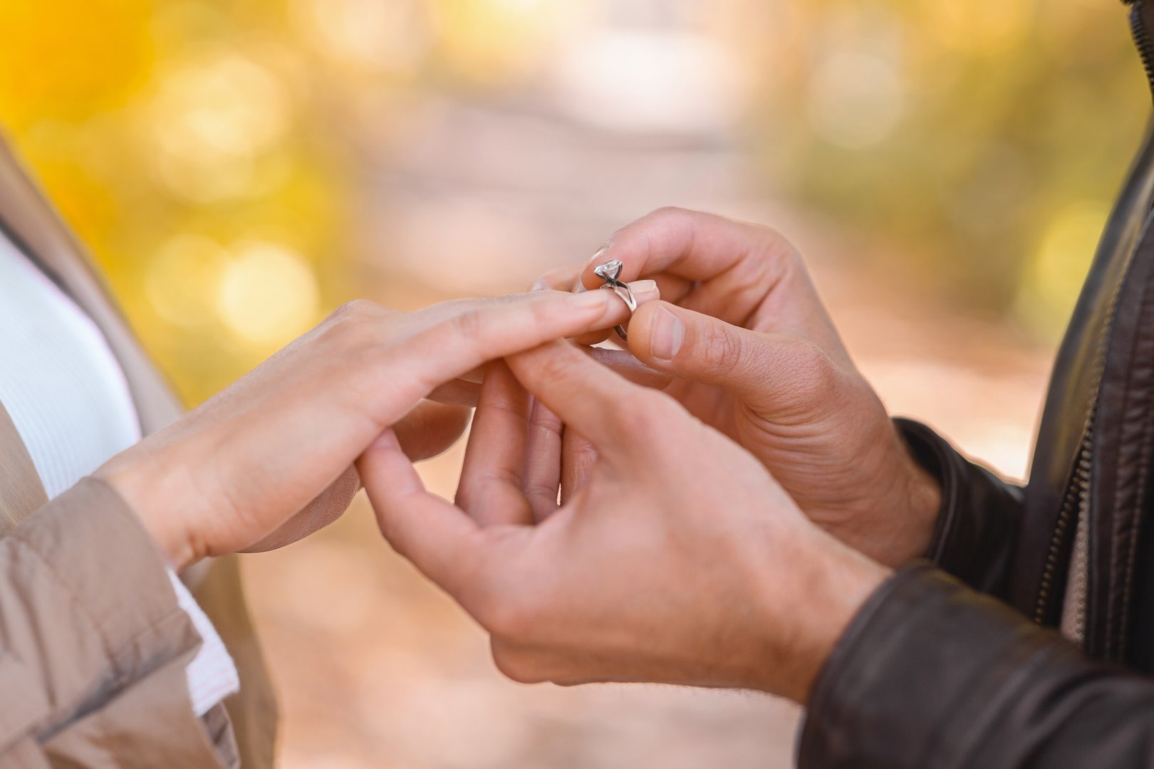 Close up of man putting engagement ring on woman's hand over blurred autumn forest background