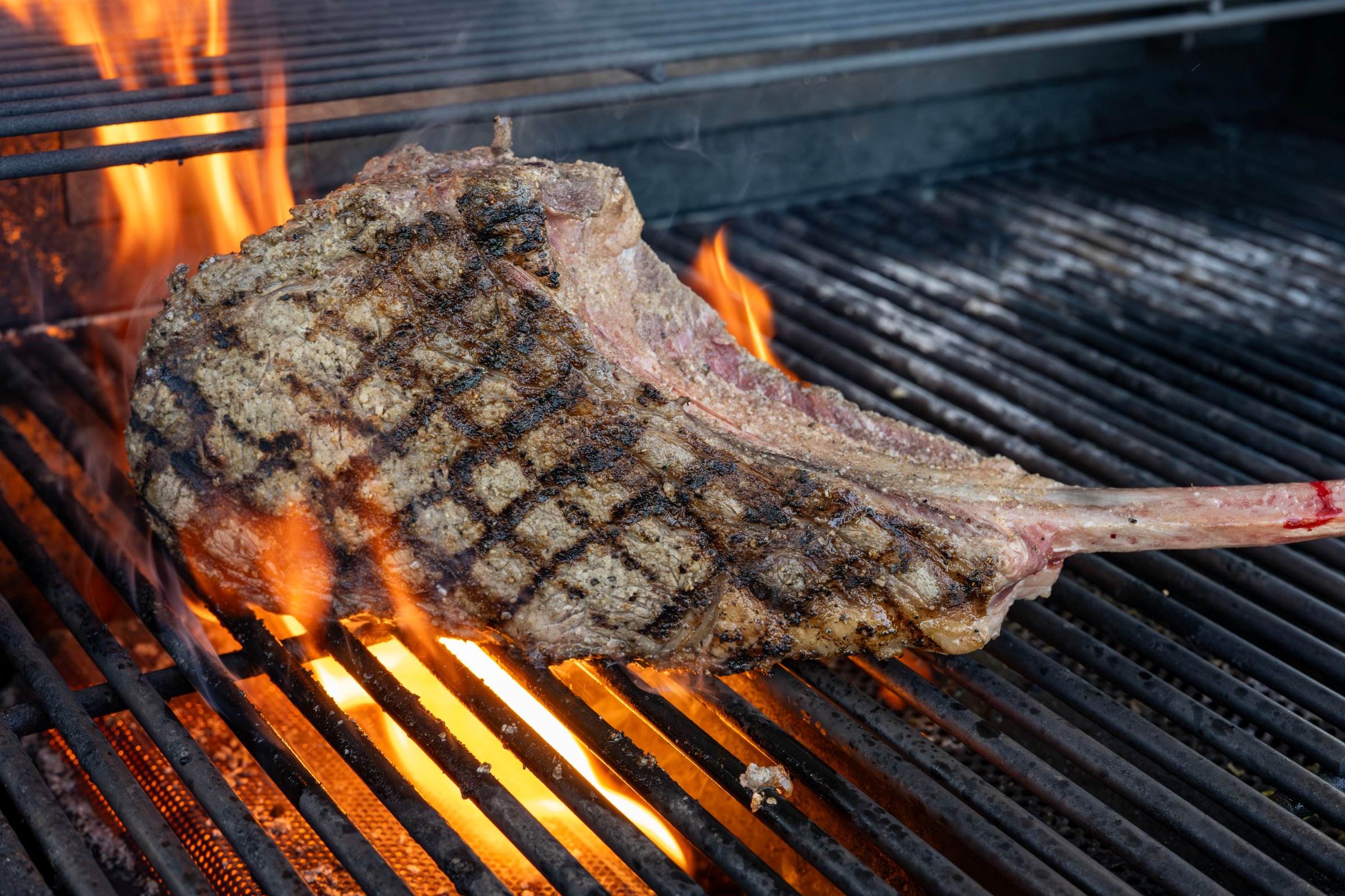 A tomahawk steak flaring up on the grill