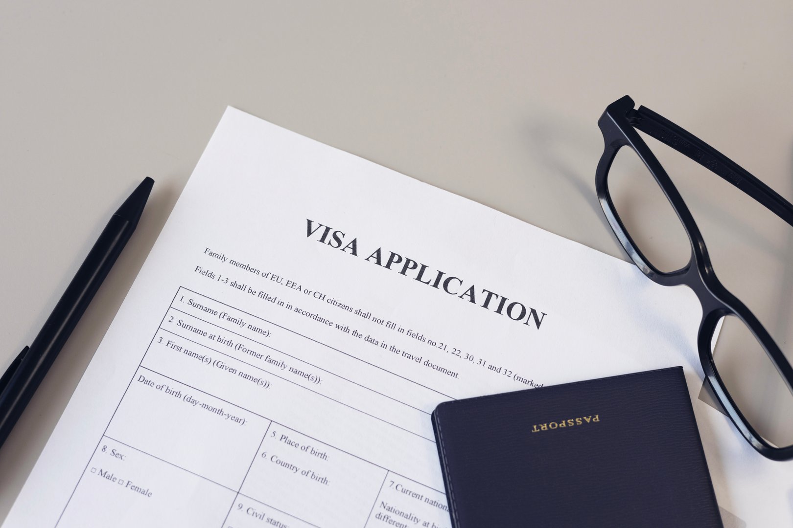 Visa application form, pen, eye glasses and passport on desk.