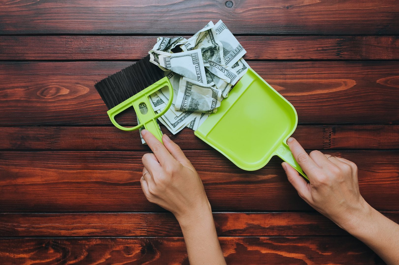 Two female hands hold a brush and scoop and remove dollar bills from the wooden table. The concept of devaluation, depreciation, inflation and default, when money loses its value.