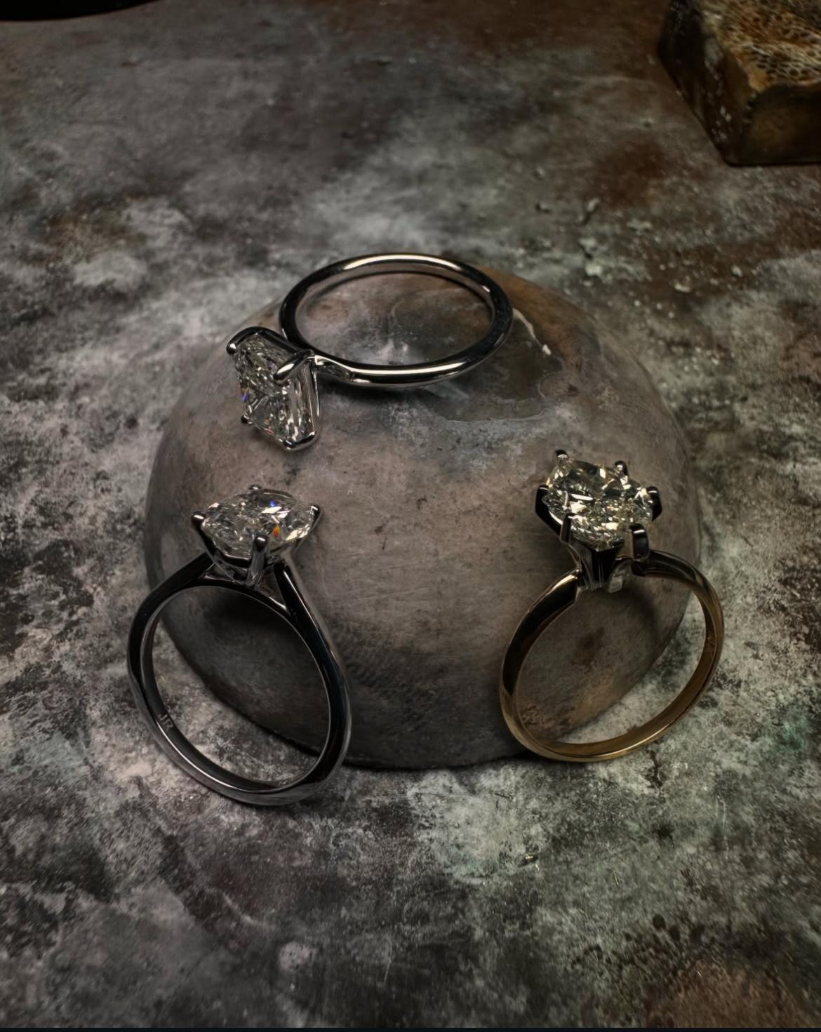 Four engagement rings with large gemstones displayed on a textured surface.