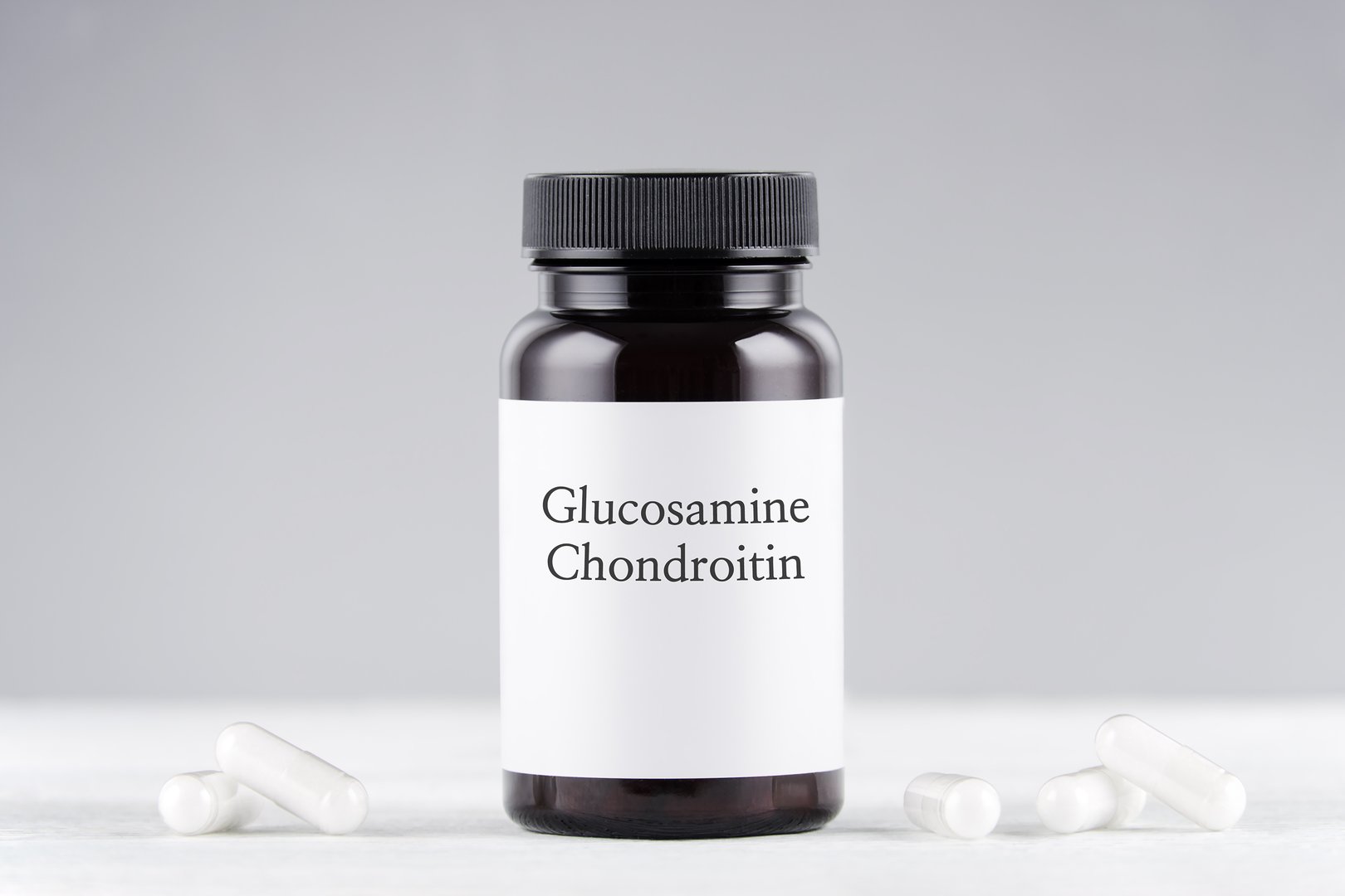nutritional supplement glucosamine and chondroitin bottle and capsules on gray background