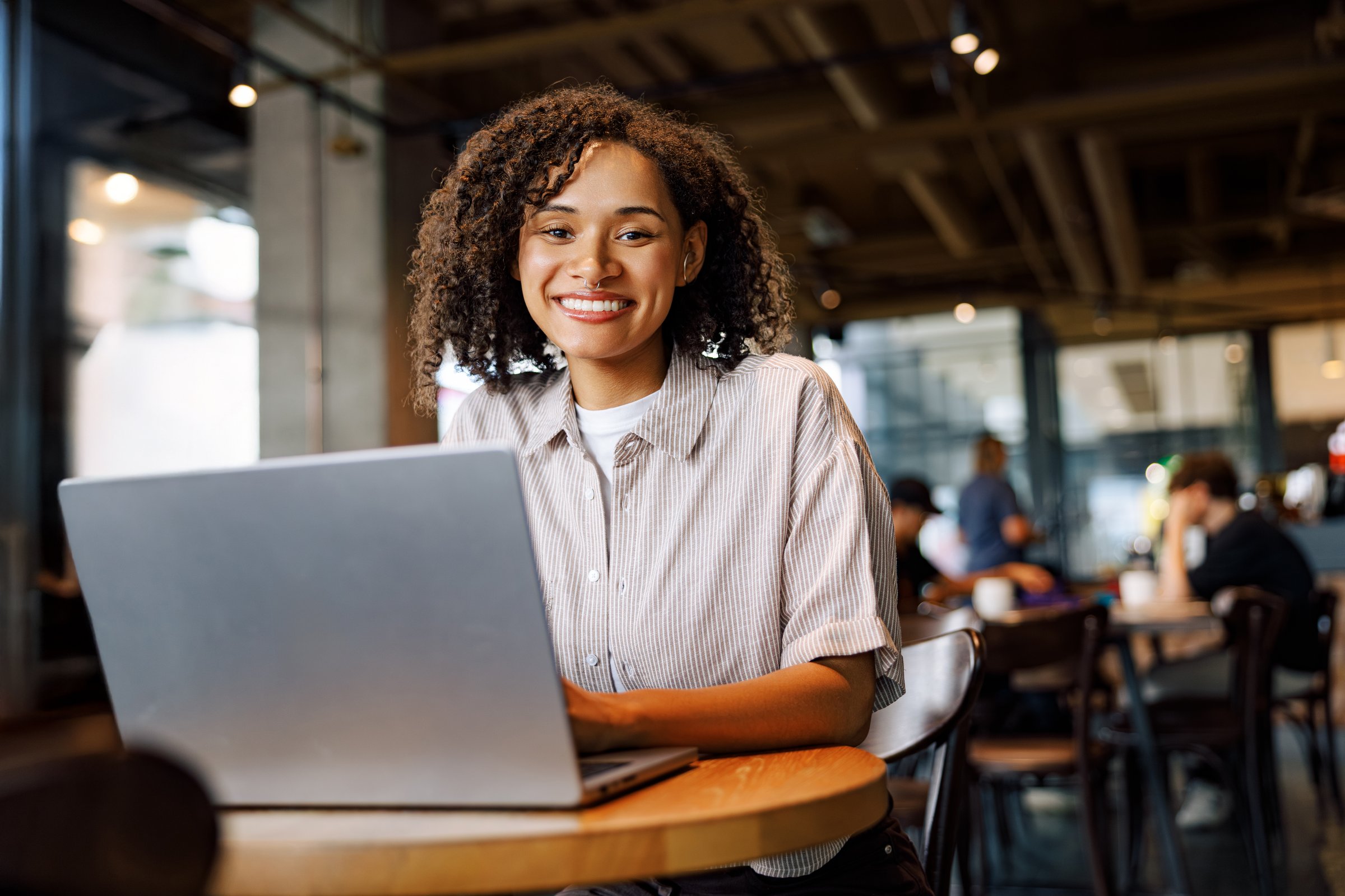 A smiling woman engaged in work on her laptop in a stylish cafe, showcasing productivity and relaxation.