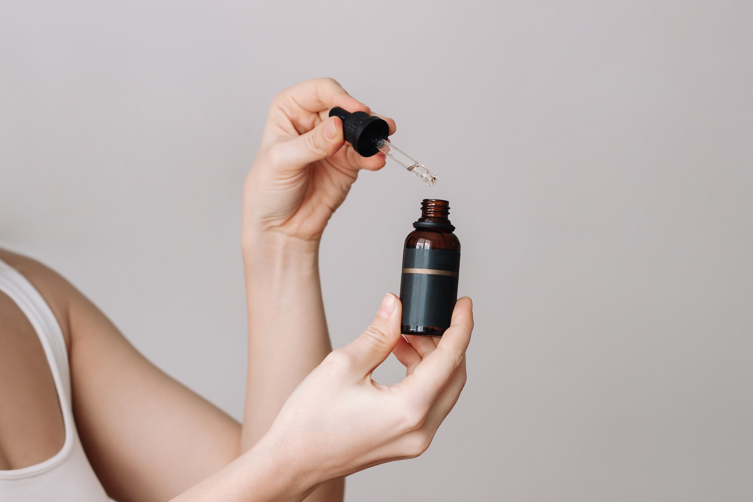 Young woman holding a dropper and a glass bottle with essential cosmetic oil on a gray background. Skin care. Cosmetology beauty concept