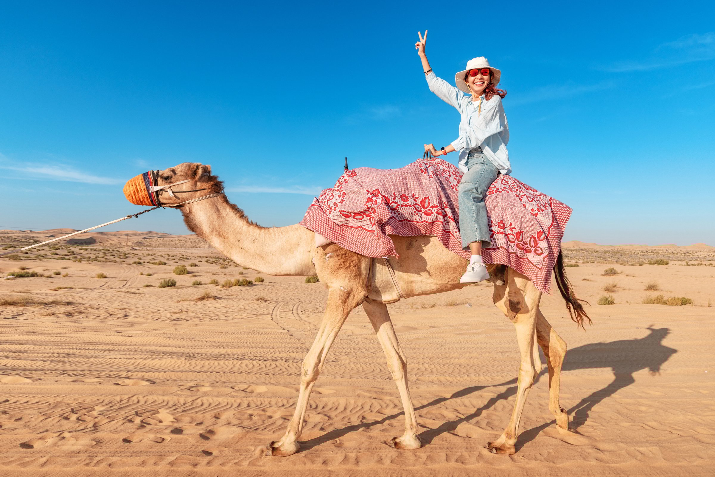 Smiling female tourist riding a dromedary camel in the desert during a sunny day