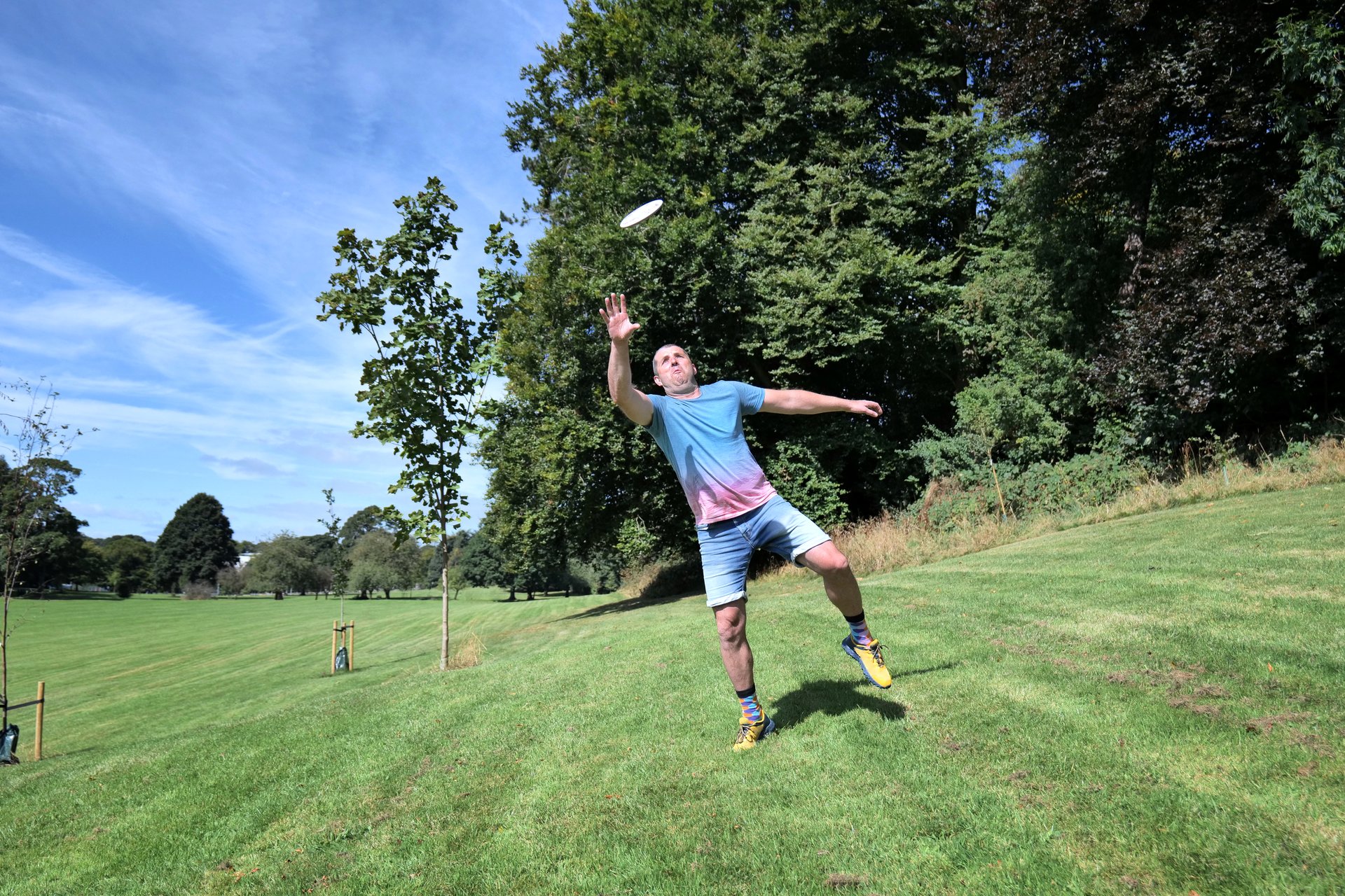 A fit and healthy middle-aged white man readies to make an energetic leap to grab a white rubber flying disc during summer games in the park.