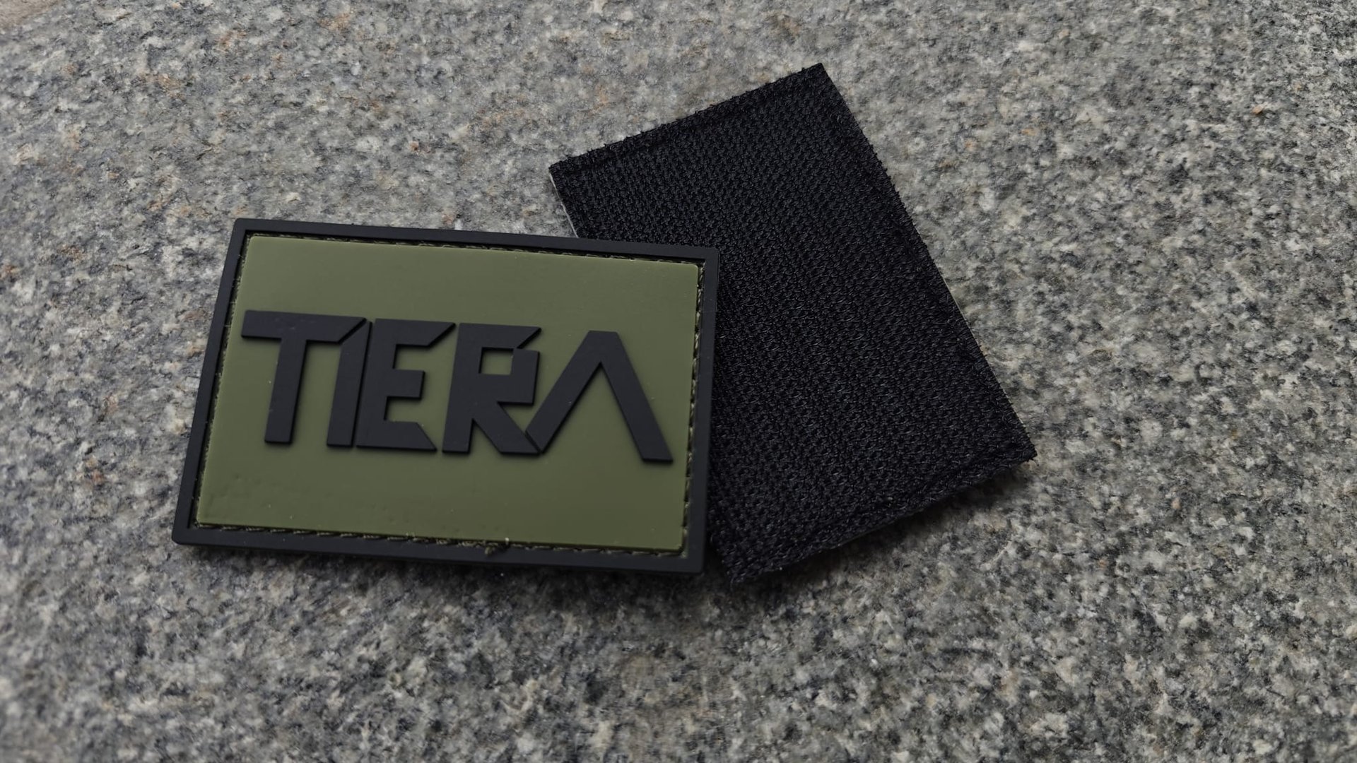 A green patch with TIER in black letters, accompanied by a black backing, placed on a textured gray surface.