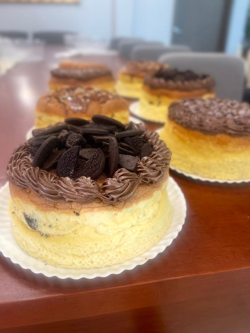 Three cheese cakes topped with chocolate frosting and cookies on a wooden table.