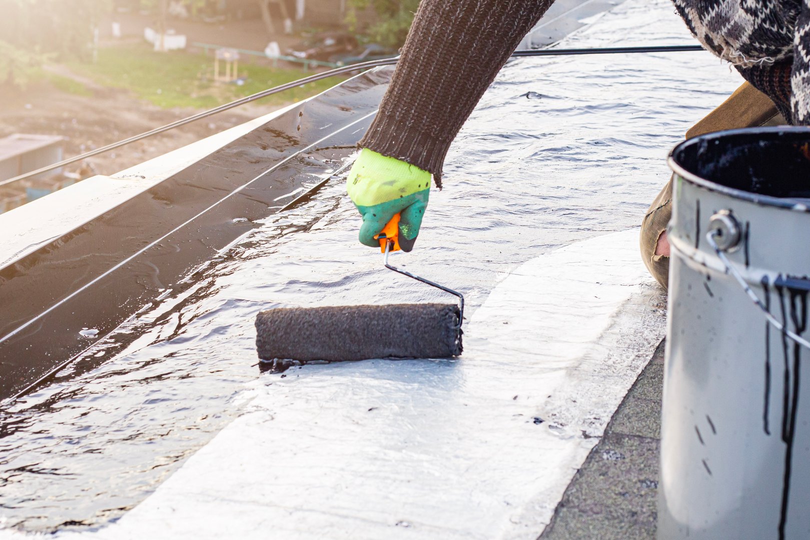 Worker treating roof with bitumen primer