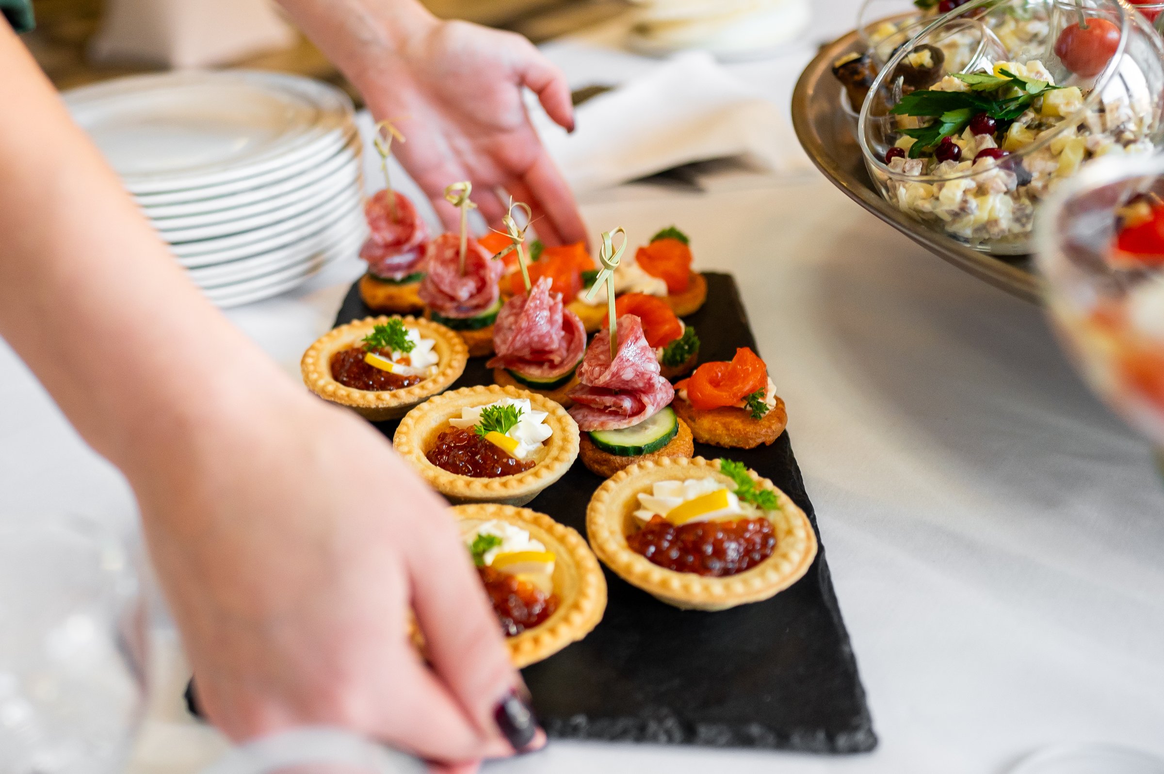 A variety of gourmet appetizers elegantly presented on a serving table, with a hand reaching for a dish. Perfect for culinary, catering, or event themes, showcasing the diversity of the food.