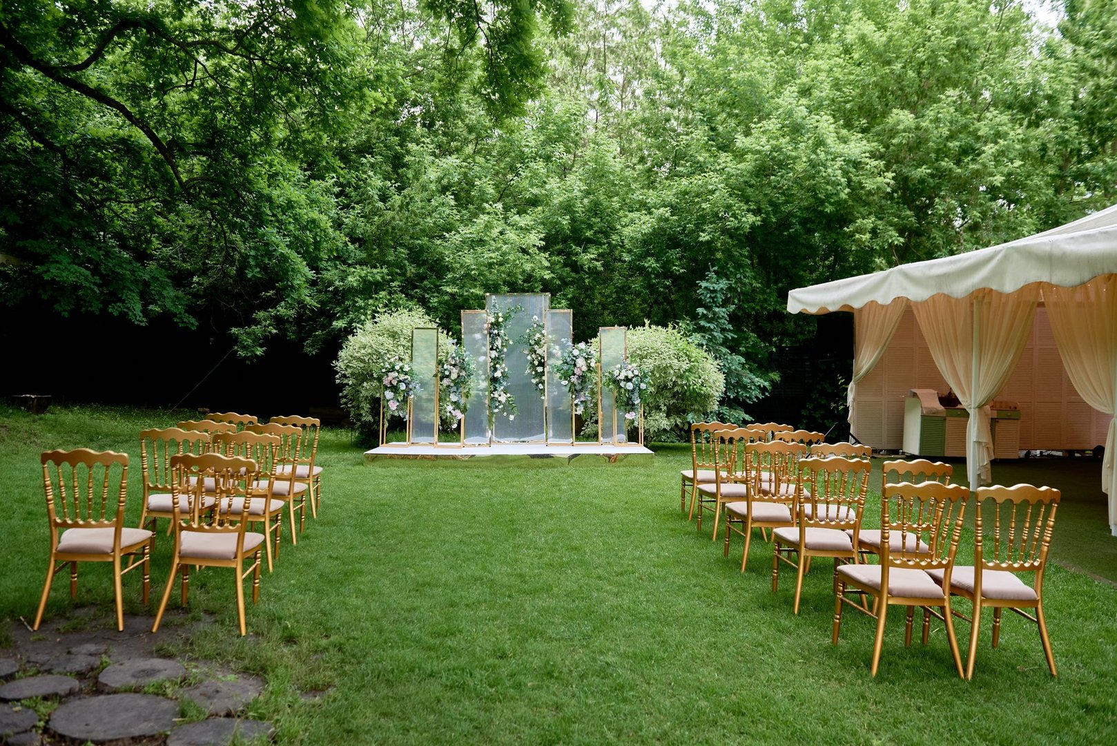 Place for wedding ceremony in garden outdoors, copy space. Wedding arch decorated with flowers and chairs on each side of archway. Wedding setting