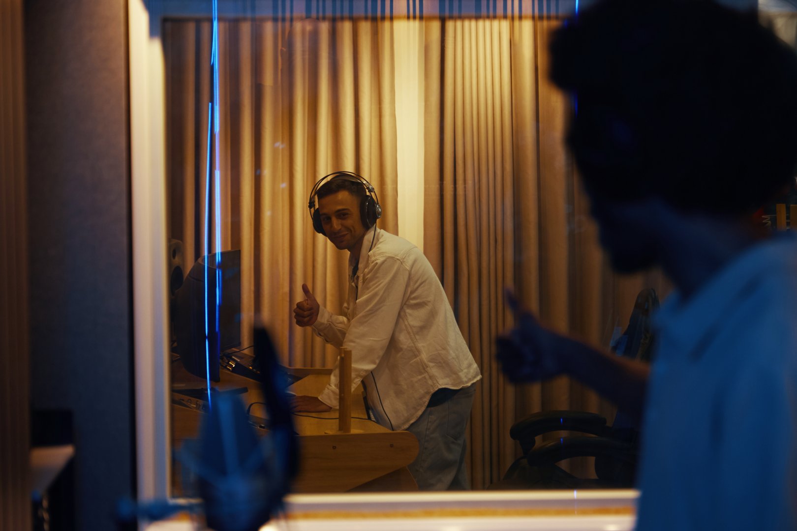Young singer standing in recording room behind the glass and showing thumbs up to composer