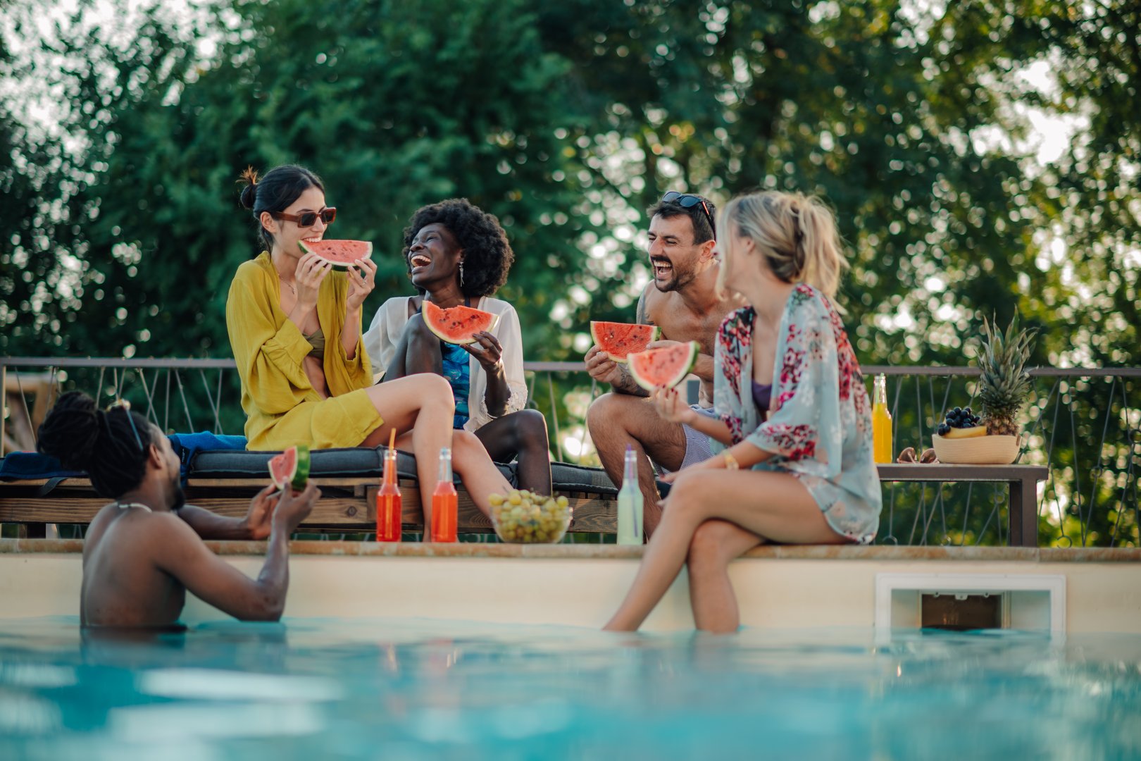 Group of friends enjoying watermelon by the poolside on a sunny day, having fun and laughing together
