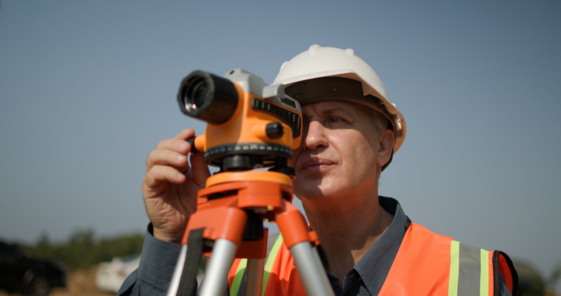 A senior male engineer is using a survey camera to measure levels on a construction site. Civil engineer utilizes a survey camera