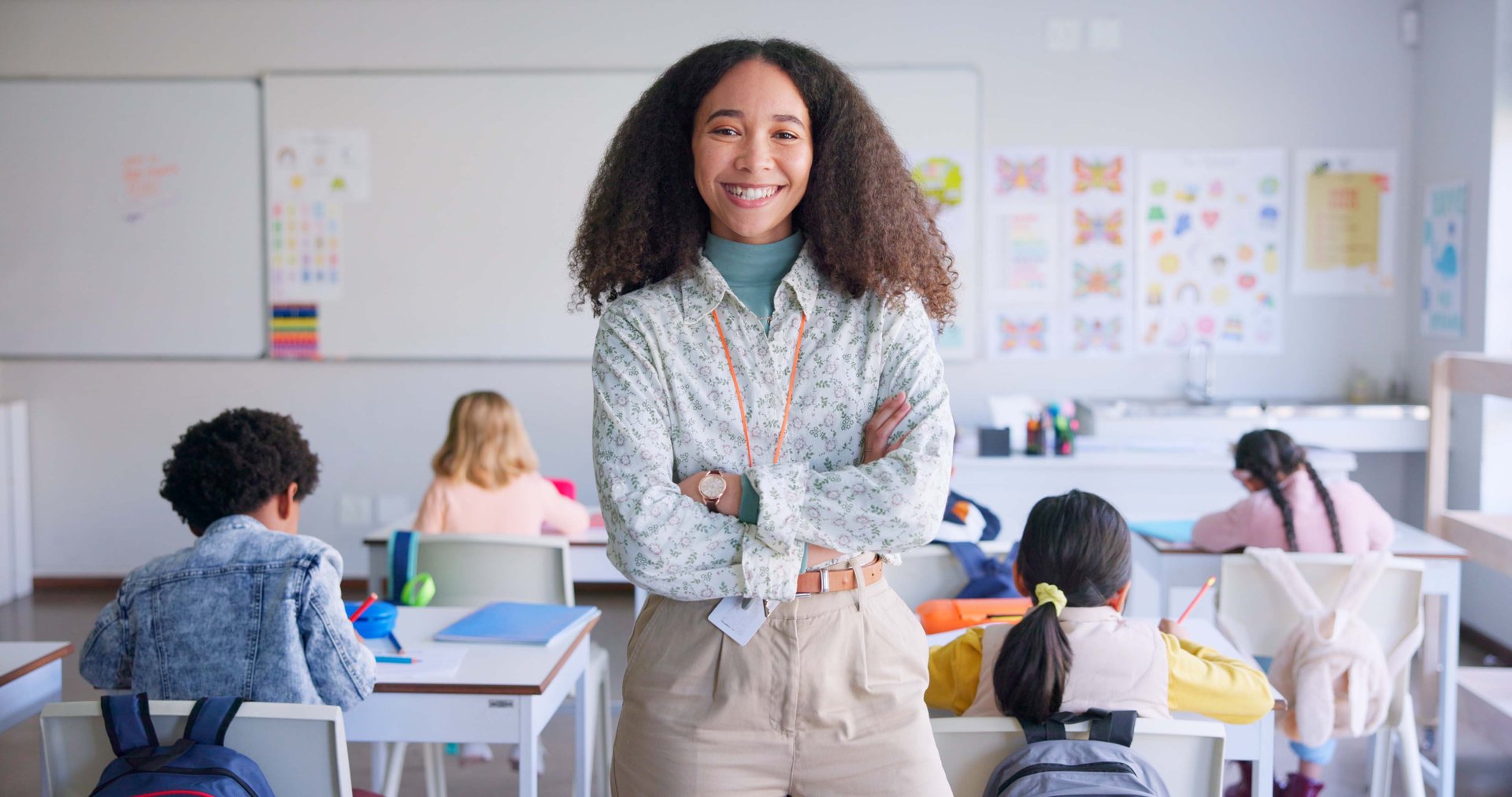Teacher woman, arms crossed and smile in class with school kids, pride or happy for education career. Academy, classroom and learning expert for children, face or portrait with development for future