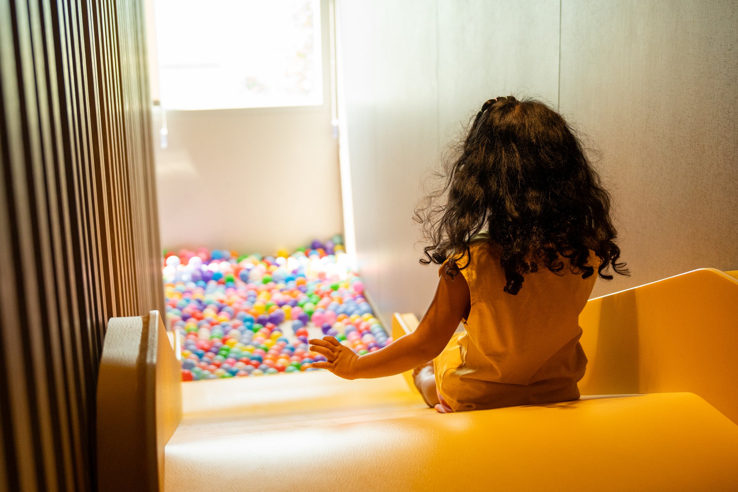 A happy little girl plays with a ball in a colorful ball pit, enjoying the fun and enhancing her development through playful activities and exercise.