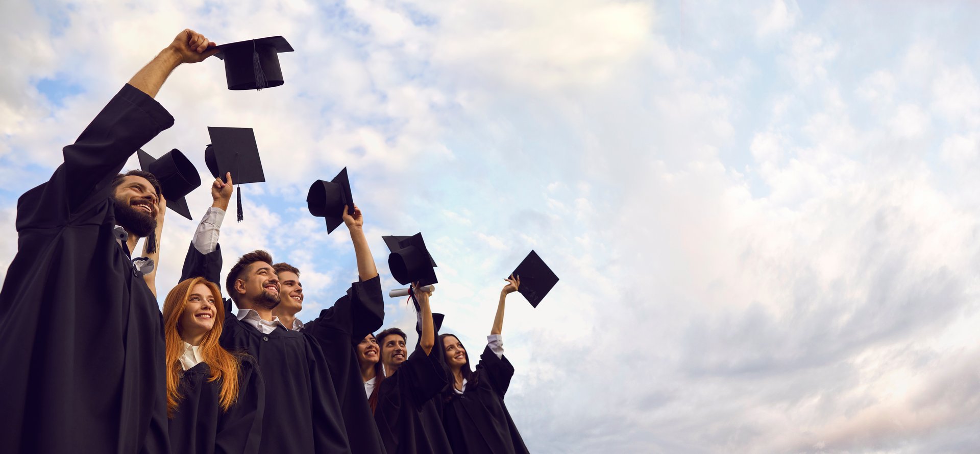 Millennial students celebrating graduation ceremony and throwing their caps up outdoors, copy space text. Young people on commencement day