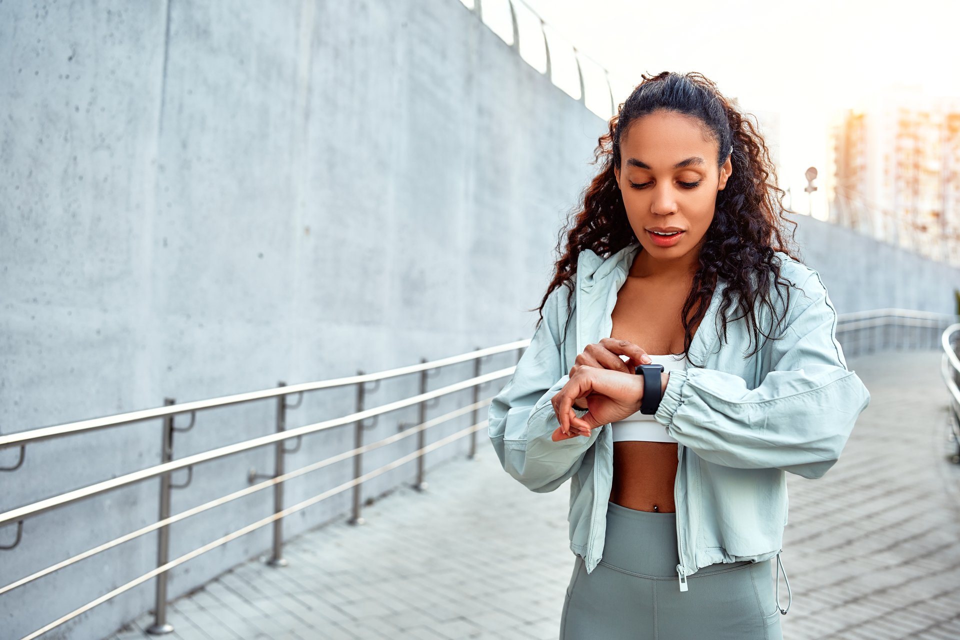 Beautiful african american woman in sports clothes checking pulse in smart watch. Attractive athlete using smart watch. Sport and technology concept. Morning running and workout.