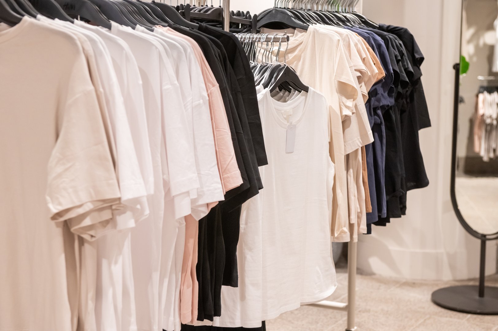 Various t-shirts in neutral colors on hangers in retail clothing store. Fashion photography for design, poster, and store display