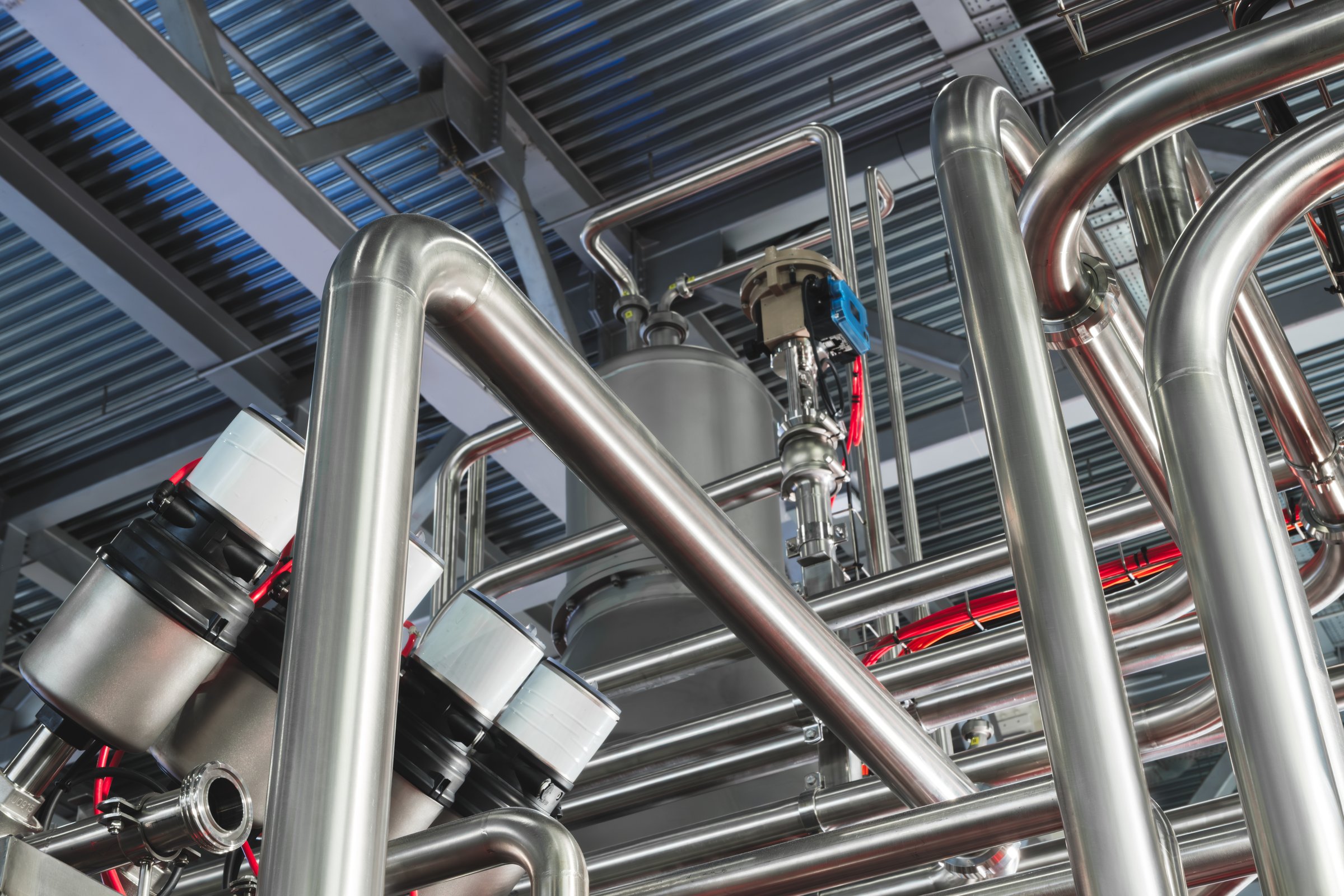 Stainless steel pipes attached to stainless steel tank with industrial food production machine, industrial concept background.