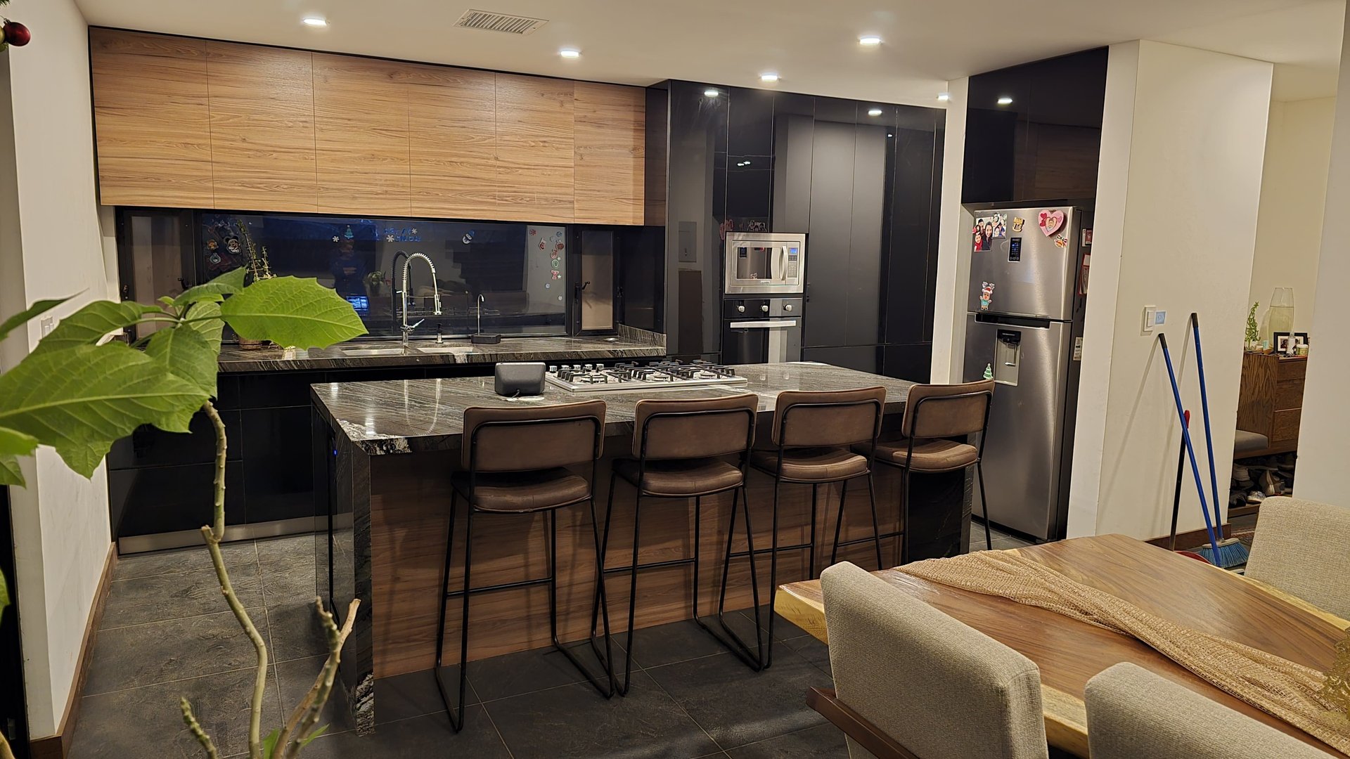 Modern kitchen with a marble island, barstools, wood cabinets, stainless steel appliances, and adjacent dining area.