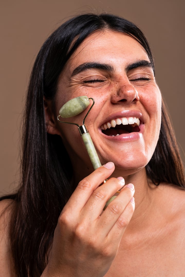 Cheerful young woman enjoying a relaxing face massage with a jade roller, radiating happiness while experiencing the soothing benefits of her skincare routine