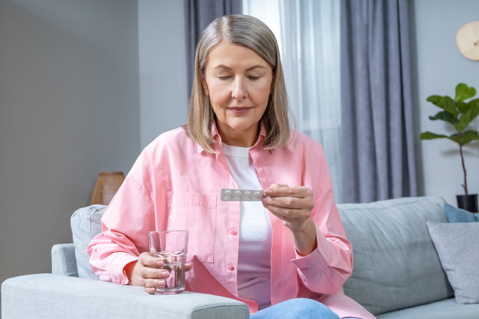 HRT. Mid aged woman in pink shirt taking HRT pills
