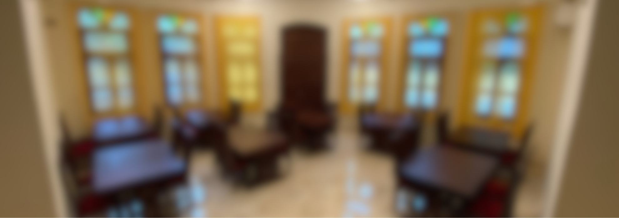 Blurry image of a room with large windows and several tables with chairs, featuring bright yellow walls and marble flooring.