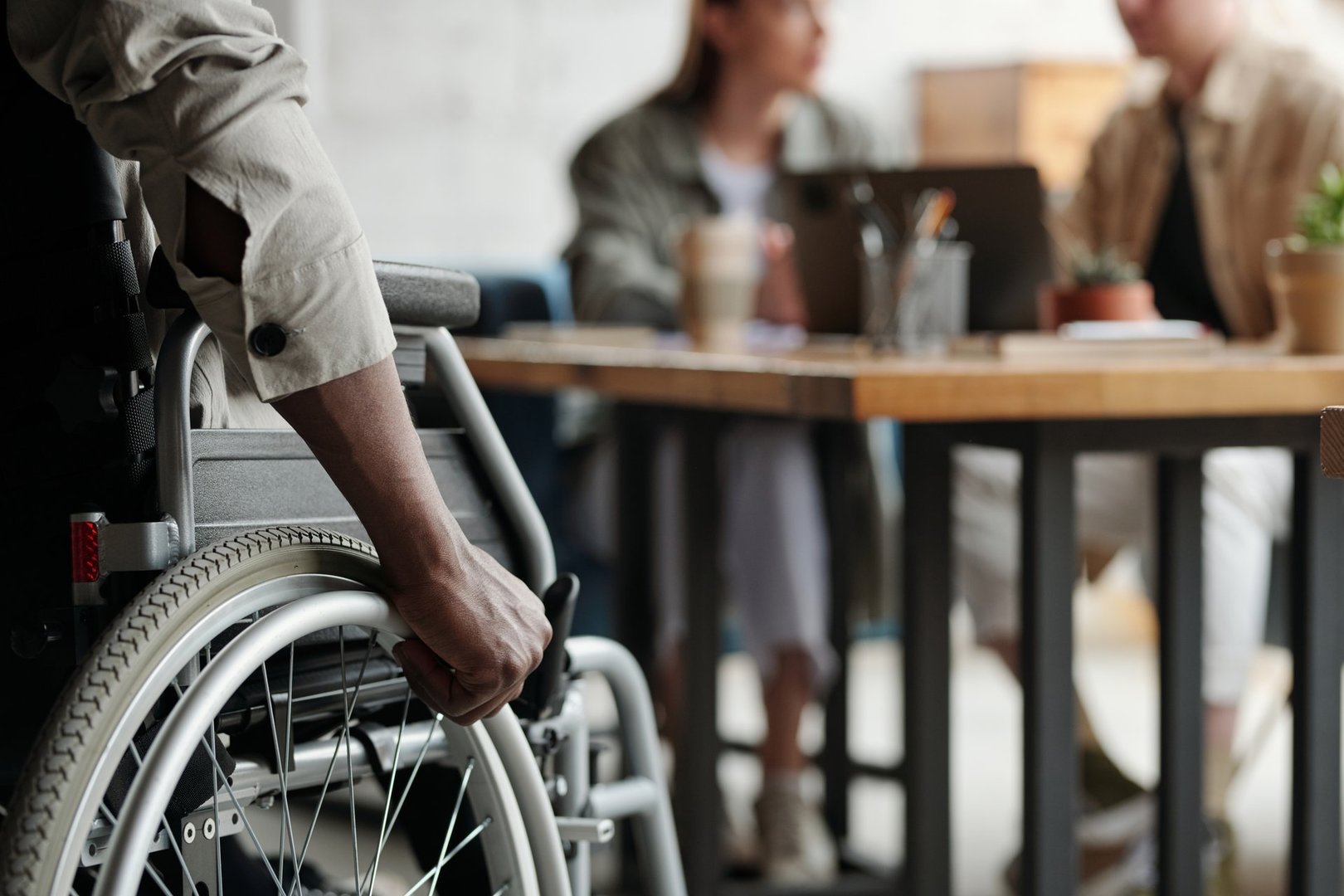 Part of young African American male employee with disability keeping hand on wheel of wheelchair while moving towards his colleagues
