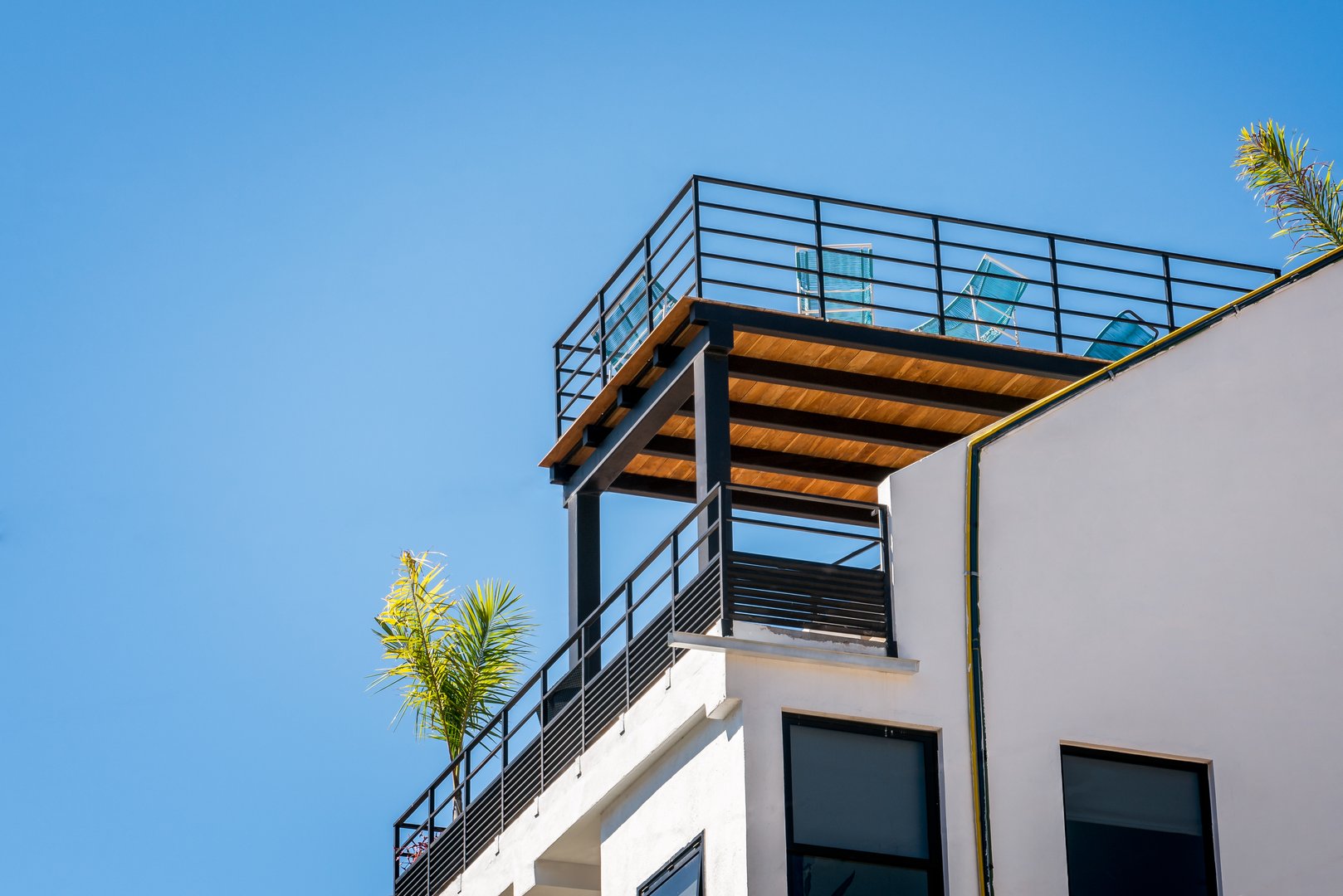Rooftop terrace and balcony with patio furniture and plants against a clear blue tropical sky. Residential