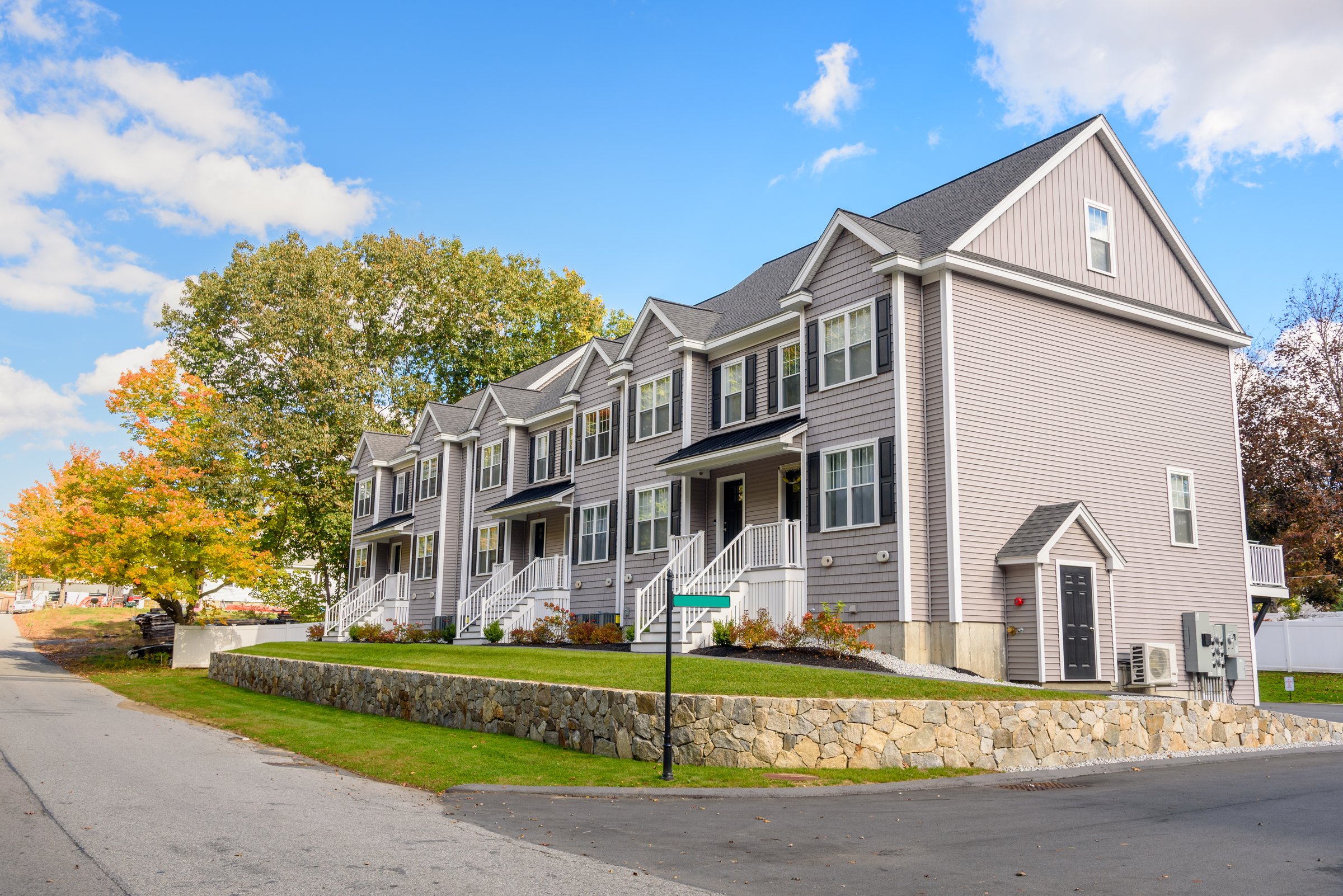 Newly built row houses in a housing development under blue sky in autumn. Colourful autumnal trees are in background. Lowell, MA, USA,