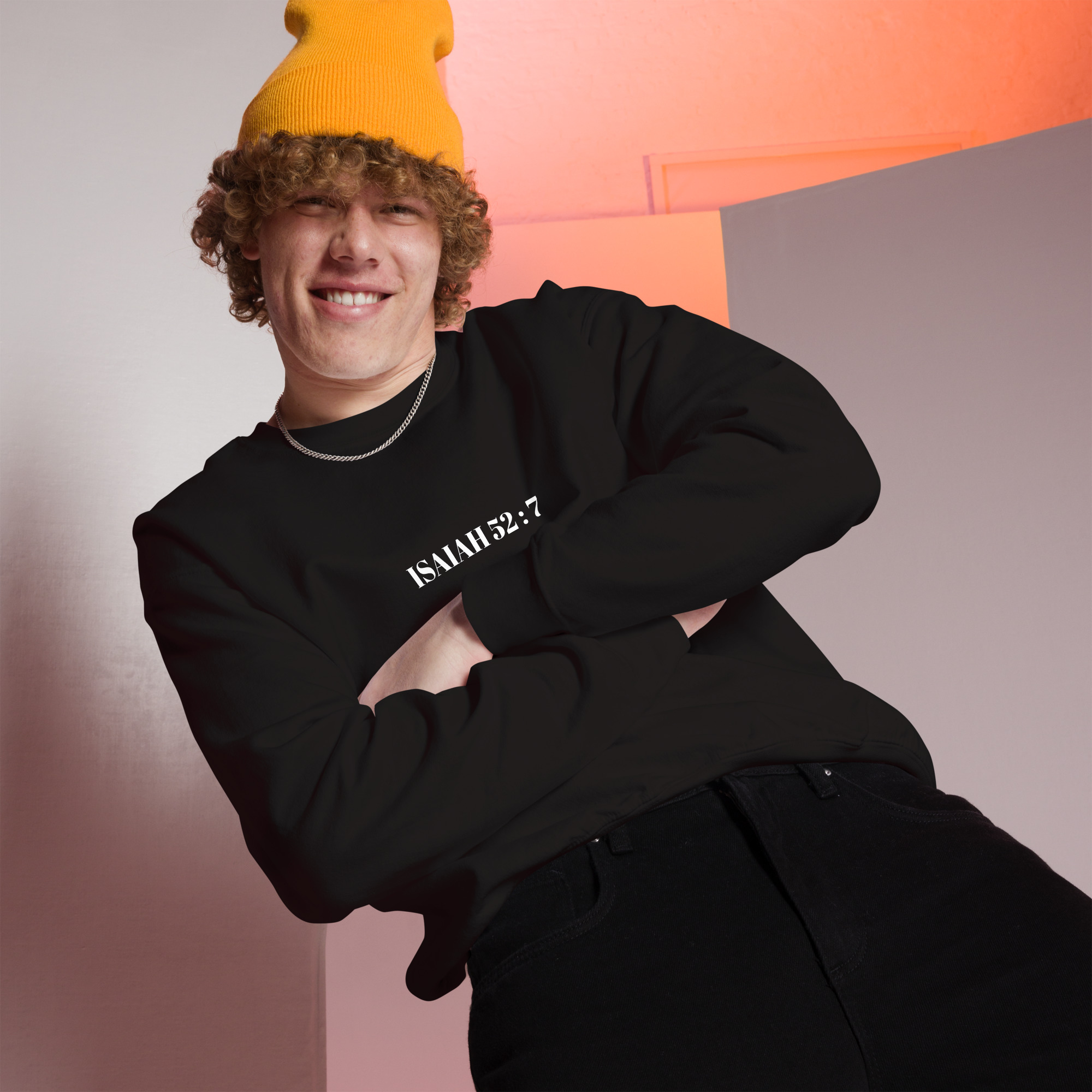 Young man wearing a yellow beanie and black sweater with "ISAIAH 35:7" printed on it, posing in a modern indoor setting.