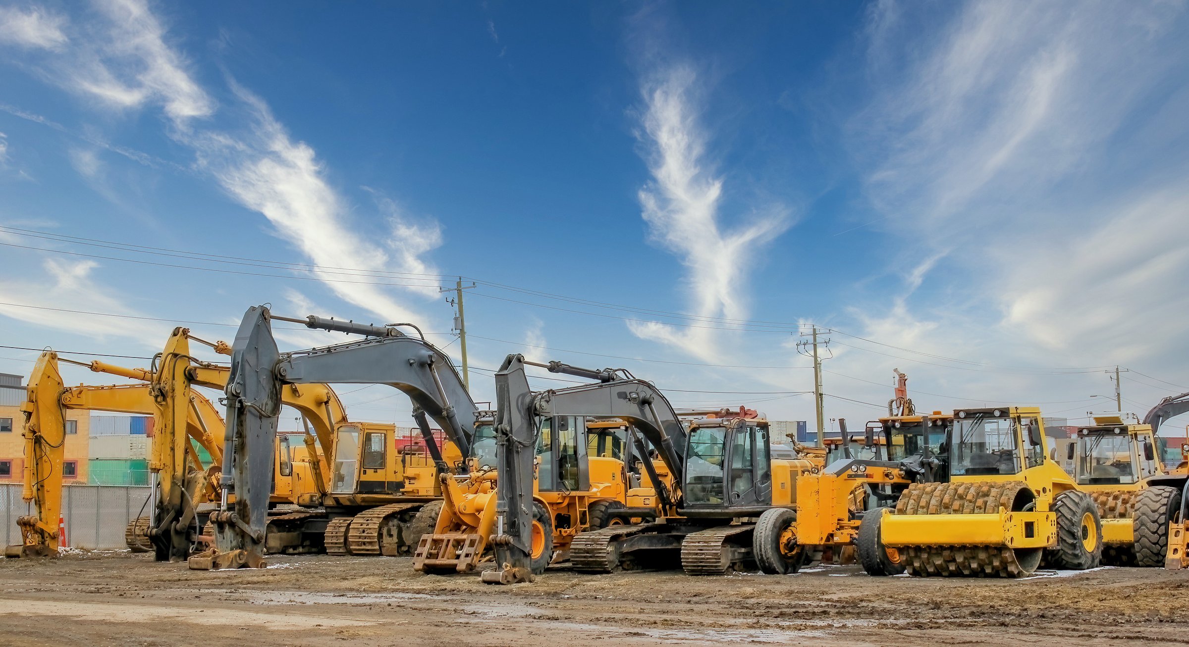 Various heavy construction vehicles, such as excavators, diggers, earthmovers, and bulldozers, are stationed at a construction site throughout the winter season.