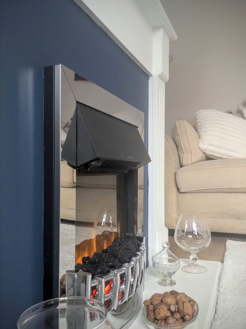 Cozy living room with a modern fireplace, beige sofa, and a table with a glass of nuts and decorative items.