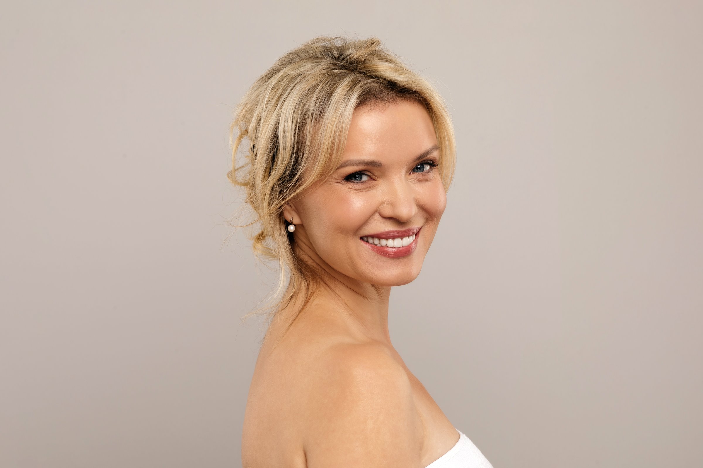 Closeup Portrait Of Smiling Attractive Middle Aged Woman With Bare Shoulders Posing Over Grey Studio Background, Happy Mature Lady With Beautiful Aged Skin Looking At Camera, Copy Space. High quality photo