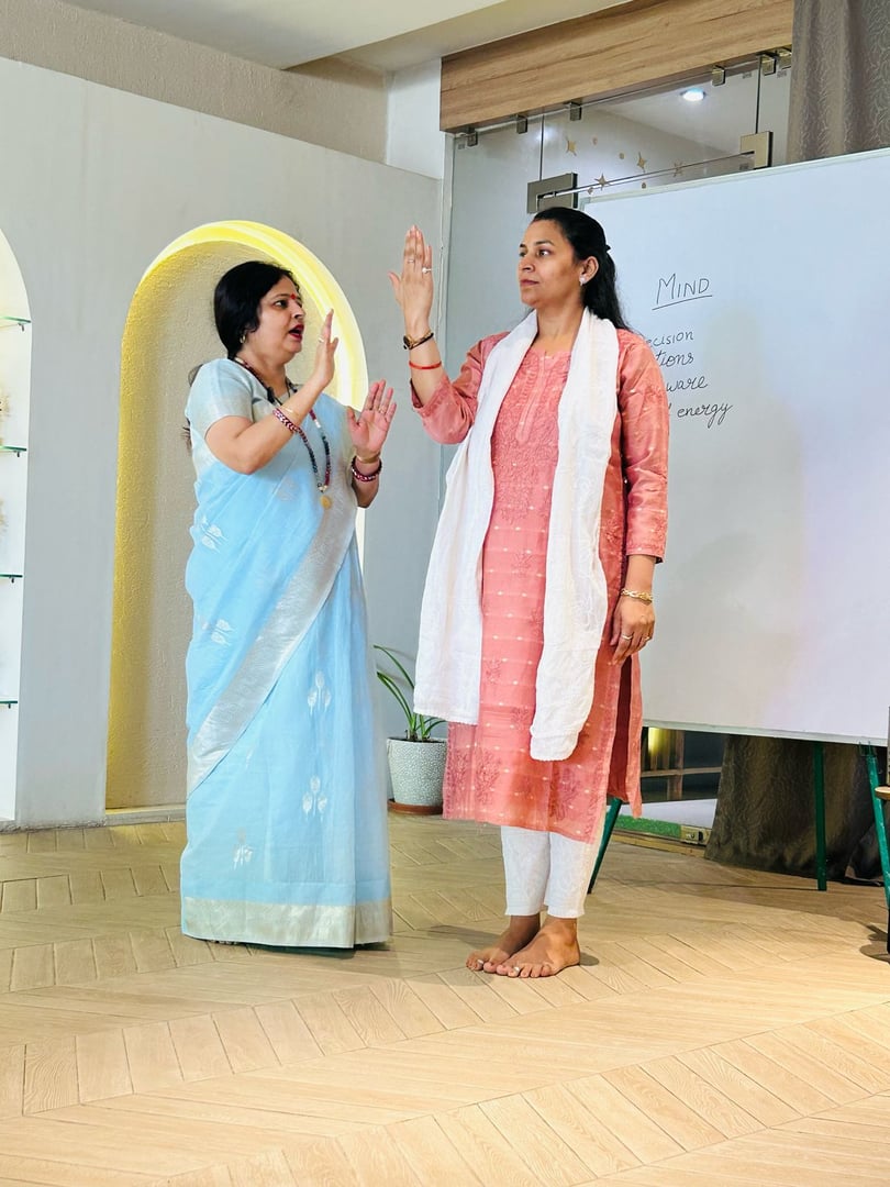 Two women in traditional attire stand near a whiteboard gesturing, possibly discussing or instructing.