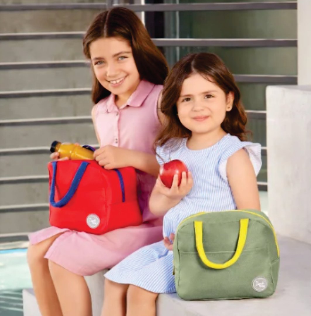 Two young girls sitting on steps holding lunch bags and a red apple, smiling outdoors.