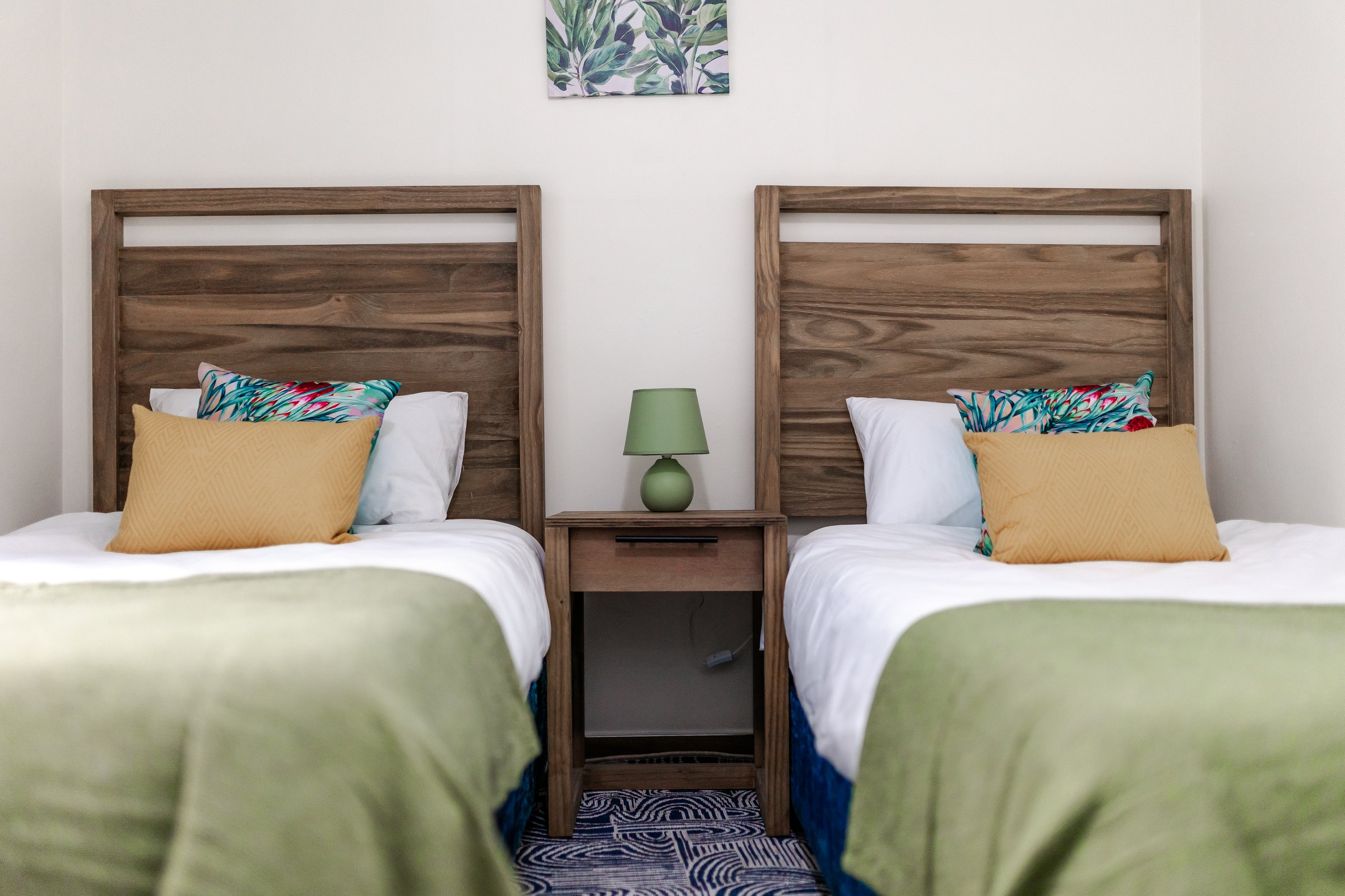 Modern bathroom with wooden vanity, round mirror, toilet, and glass shower, featuring blue and white striped blinds.